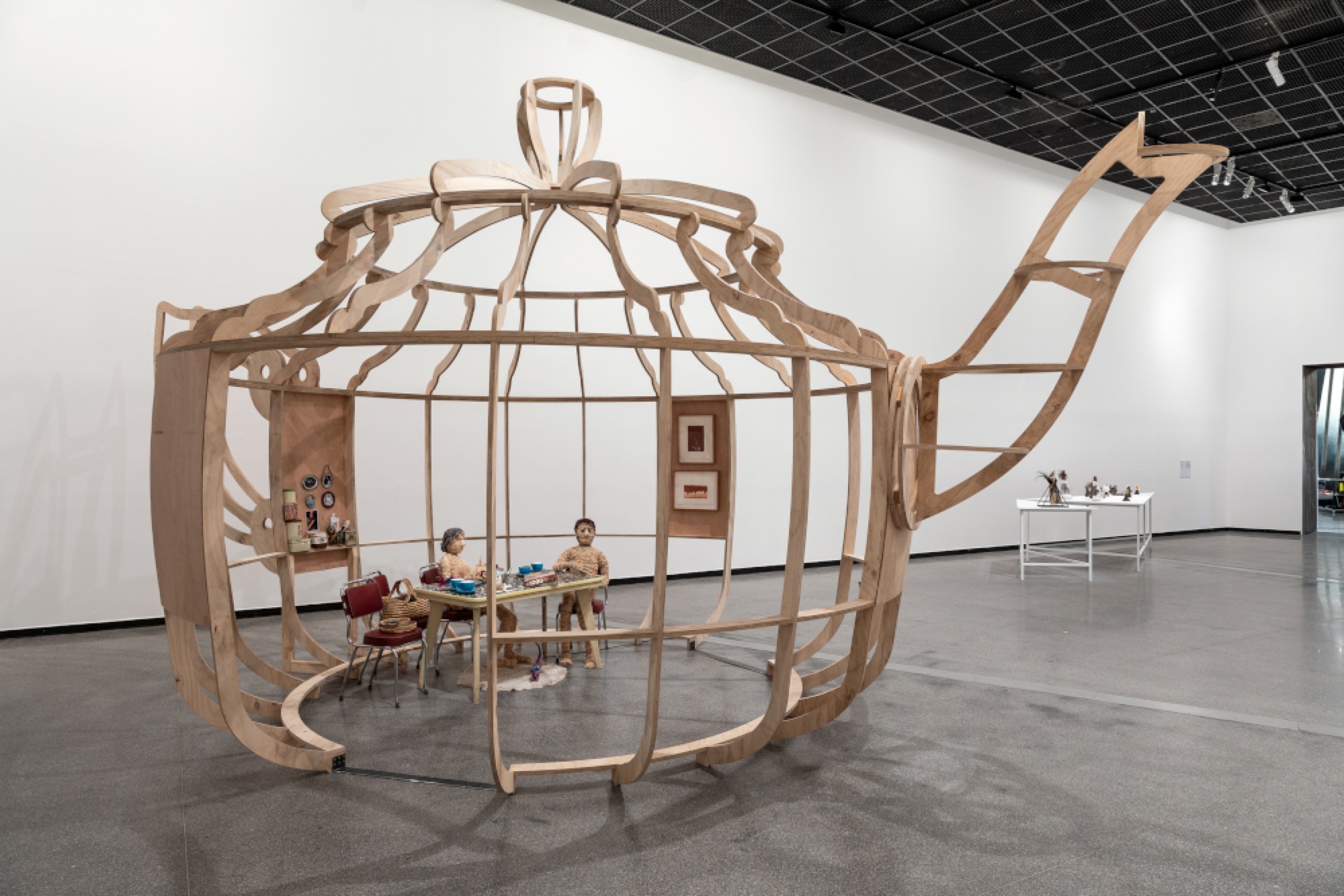 Vicki Couzens, <em>Djawannacuppatea</em> 2018, plywood, kitchen table and chairs, lamp, woven woollen matt, woven framed photographs, anodised aluminium teapot, personal collections, sound, 443.5 x 840.0 x 505.0 cm, installation view, Australian Centre for Contemporary Art, Melbourne. Sound: Robbie Bundle. Courtesy the artist. Photograph: Andrew Curtis.