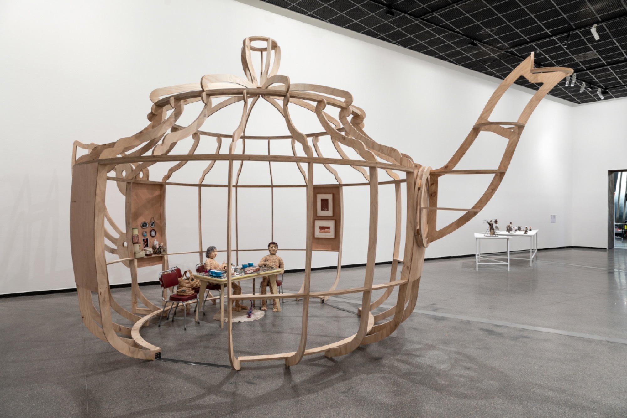 Vicki Couzens, <em>Djawannacuppatea</em> 2018, plywood, kitchen table and chairs, lamp, woven woollen matt, woven framed photographs, anodised aluminium teapot, personal collections, sound, 443.5 x 840.0 x 505.0 cm, installation view, Australian Centre for Contemporary Art, Melbourne. Sound: Robbie Bundle. Courtesy the artist. Photograph: Andrew Curtis.