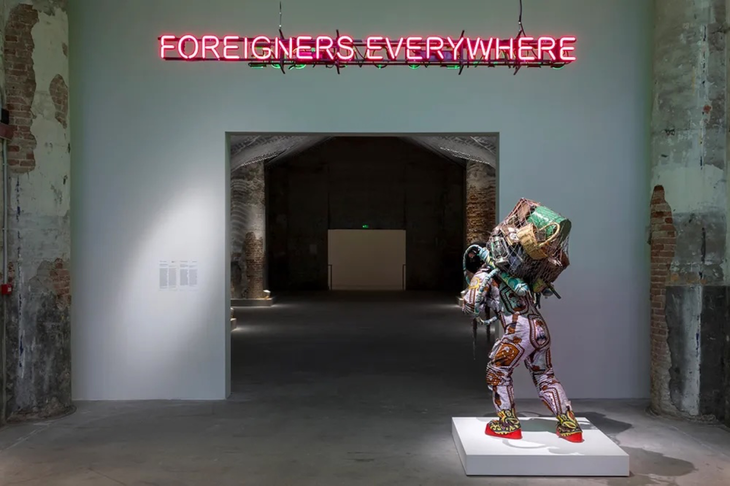 <p>Installation view of <em>Foreigners Everywhere</em> (2004–) by Claire Fontaine and <em>Refugee Astronaut VIII</em> (2024) by Yinka Shonibare at the 2024 Venice Biennale. Photography by Marco Zorzanello. Image courtesy of the artist and La Biennale di Venezia.</p>