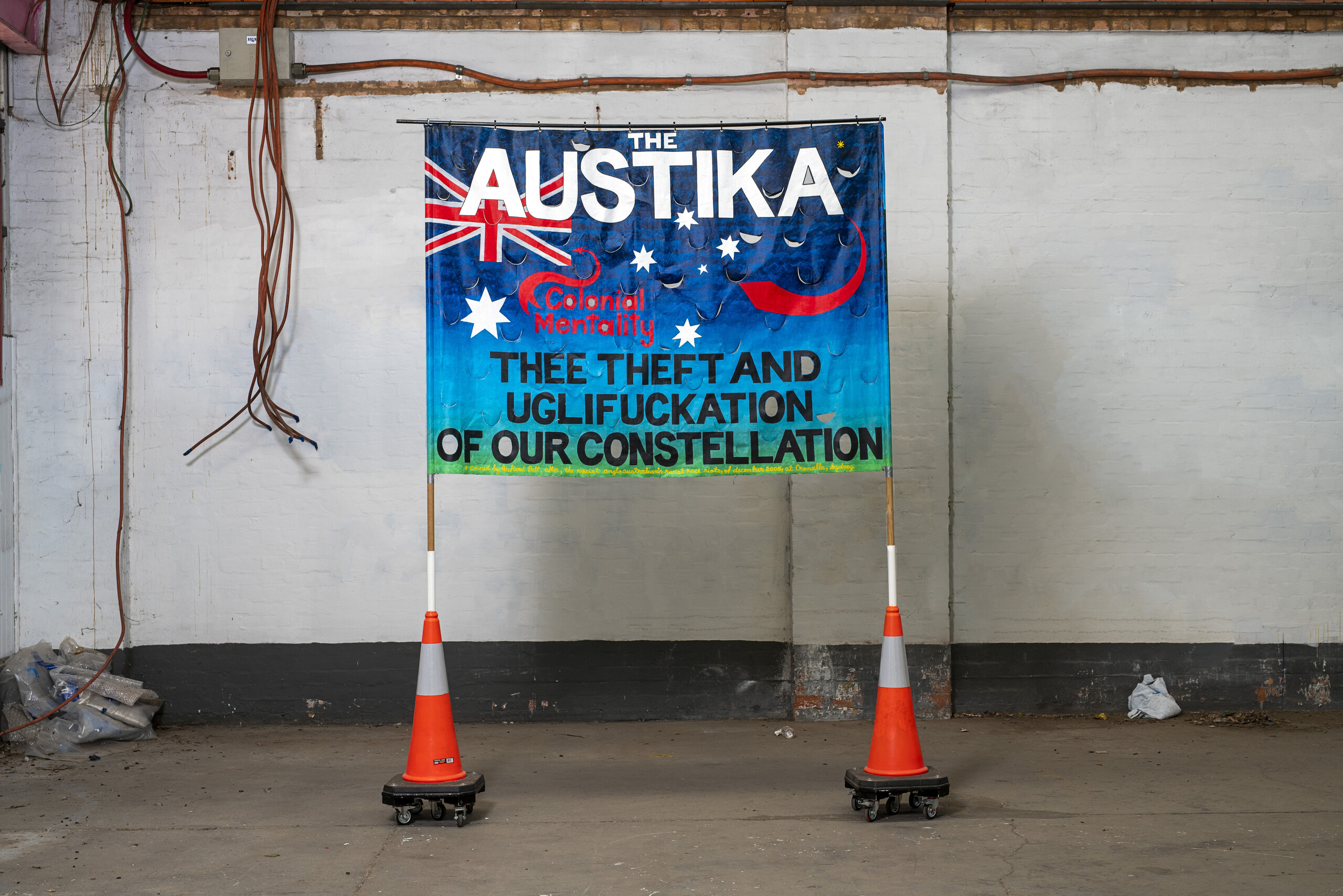 Gordon Hookey, <em>Austika/Austrailya</em>, 2020. Canvas synthetic polymer paint, metal eyelets, on wood dowels, traffic cones, castors, 300 x 265 x 50 cm. Collection: The University of Queensland, Brisbane. Photo: Rhett Hammerton. © Gordon Allan Hookey / Copyright Agency, 2022.