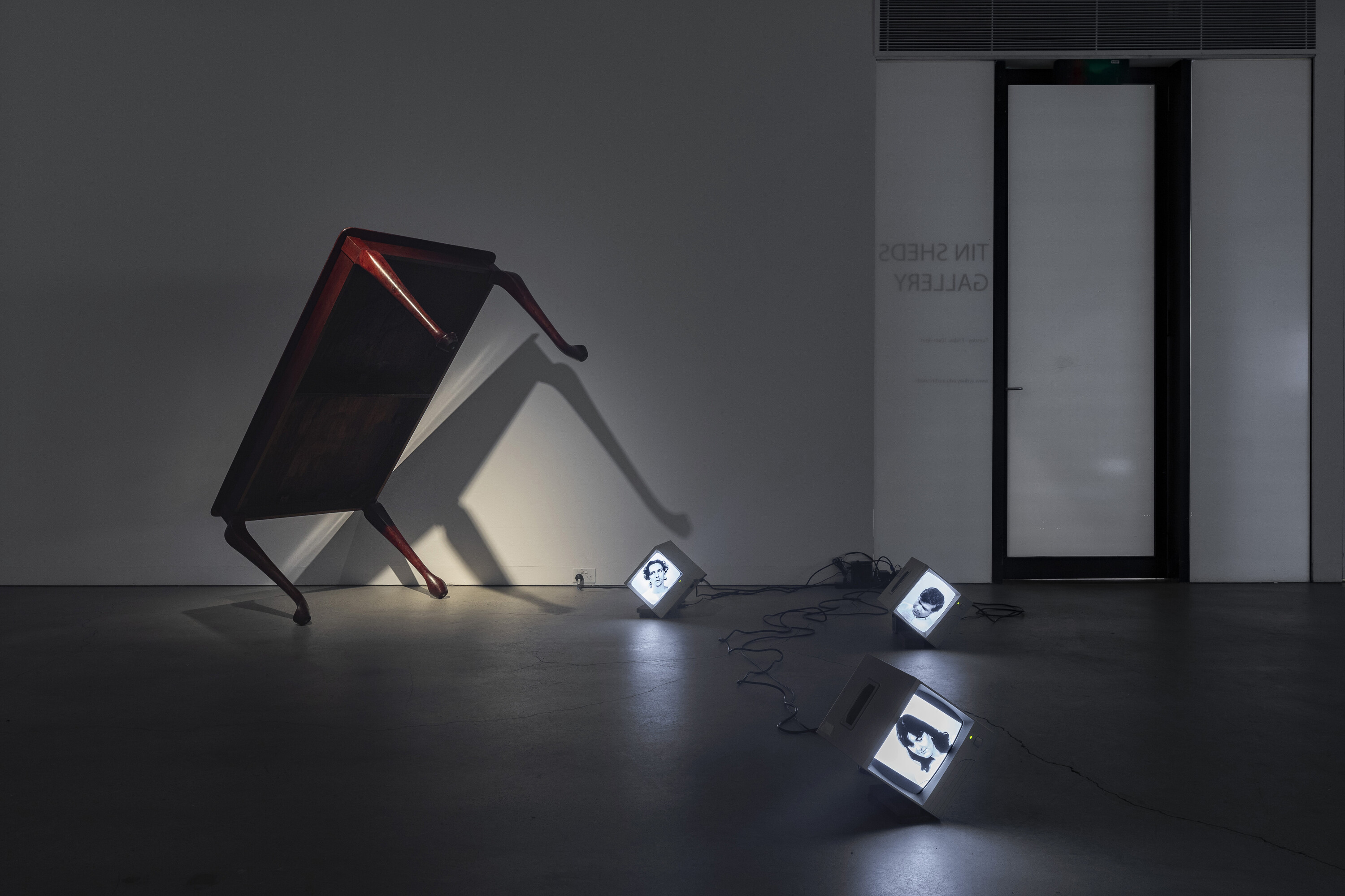 <p>Left: Denis Beaubois, <em>A Resting Weight</em>, 2024-25, Australian red cedar, maple wood table sold as Australian red cedar, dimensions variable; Right: Denis Beaubois, <em>Ellipsis</em>, 2024-25, Standard definition video, CRT monitors, Australian red cedar. Audio: List of verbs or adverbs that follow the phrase ‘Australians are’ in the Hansard transcript (Australian Federal Senate) 1901 to 1905 committed to memory, duration: seven loops, duration varies. Photo: Jessica Maurer</p>