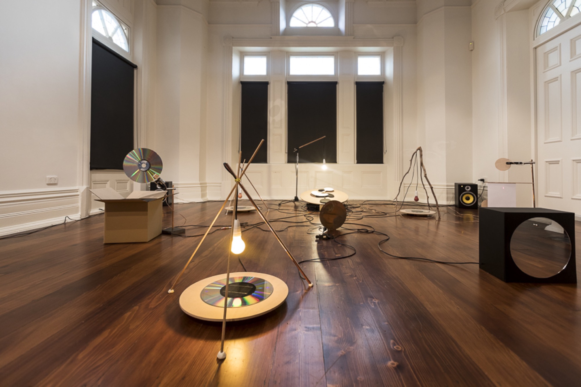 Michael G. F. Prior, <em>Open Version</em>, solar panels, laser discs, lasers, copper, bronze, microphone stand, timber, mirror, ball bearing, eucalypt branch, cardboard, paper, speakers, motors, fan, custom electronics, 2017, installation view, Bundoora Homestead, 2019 Photo: courtesy of the gallery