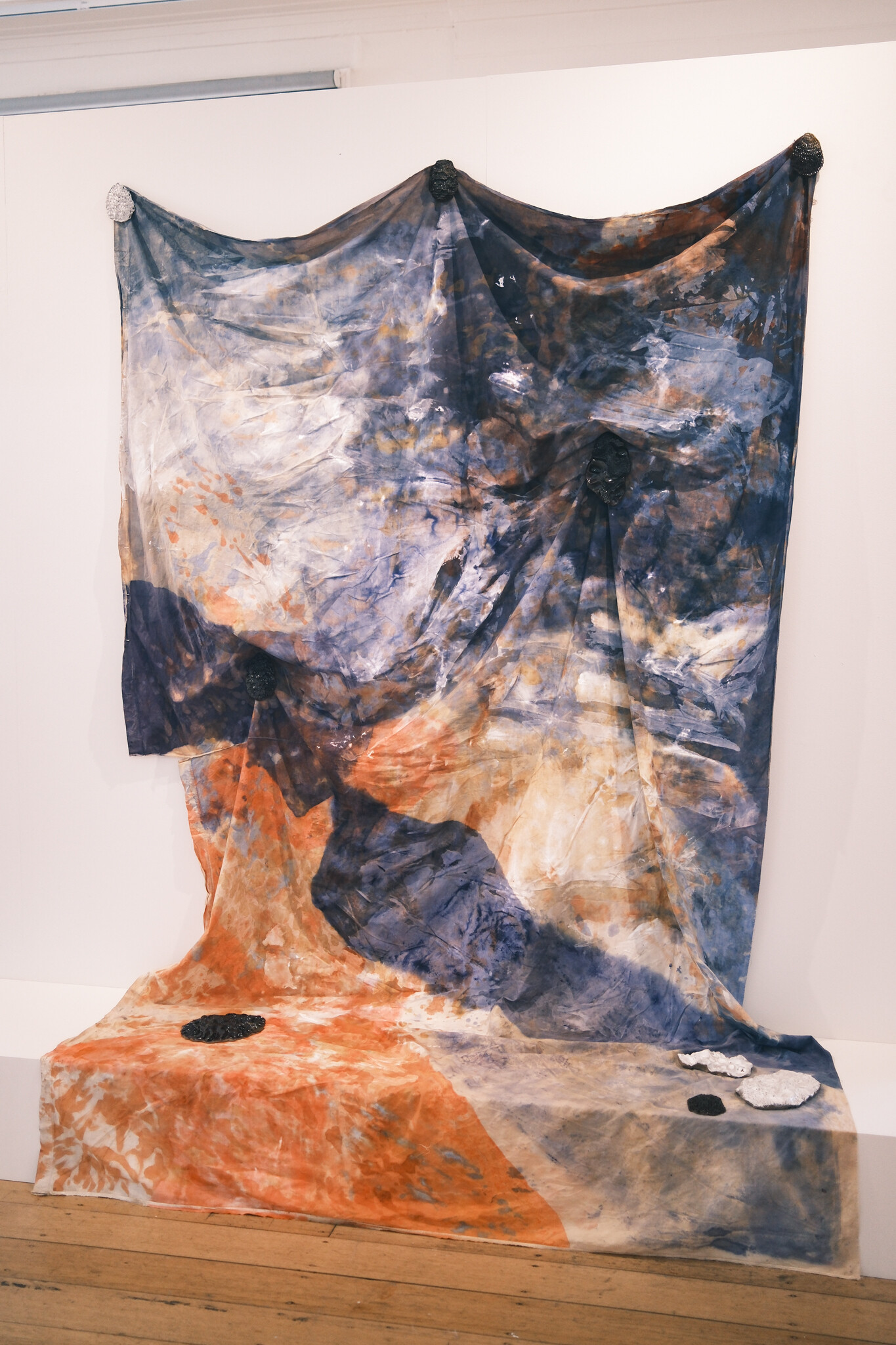 <p>Yolanda Scholz Vinall, <em>Echoing Paths</em>, 2024, avocado skins, avocado pips and red cabbage dye on recycled quilt cover with oil paint, ash and clay collected from Peramangk country, South Australia.Ceramic objects are stoneware glazed with Tenmoku or white glaze with ash. Dimensions variable. Photo: Tom Hvala</p>